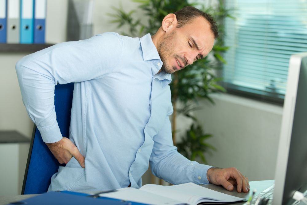 man with back pain in armchair at office