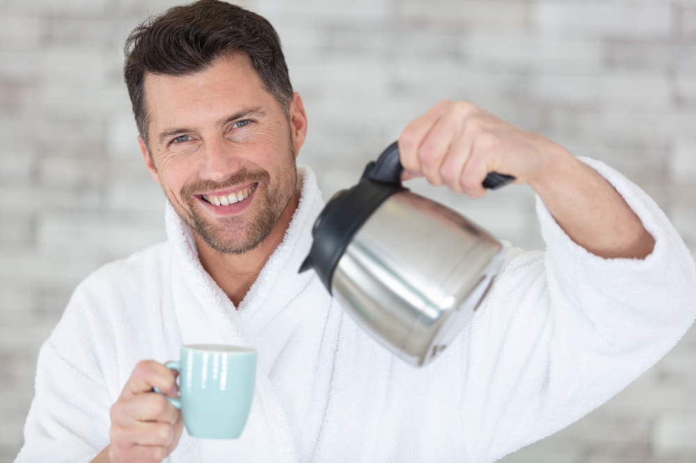 bearded young man is drinking coffee and looking at camera