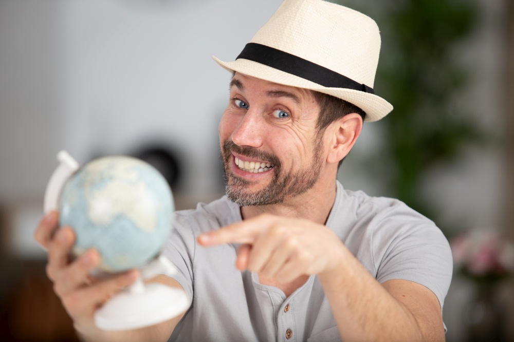young cheerful man in casual clothes pointing at globe