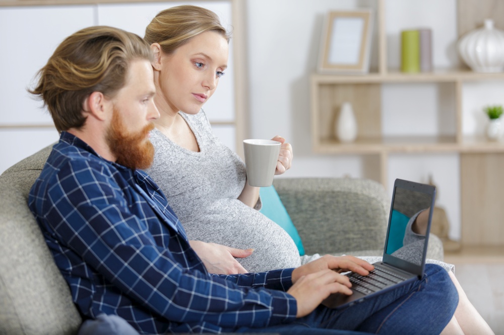 happy man and pregnant wife with pc computer at home