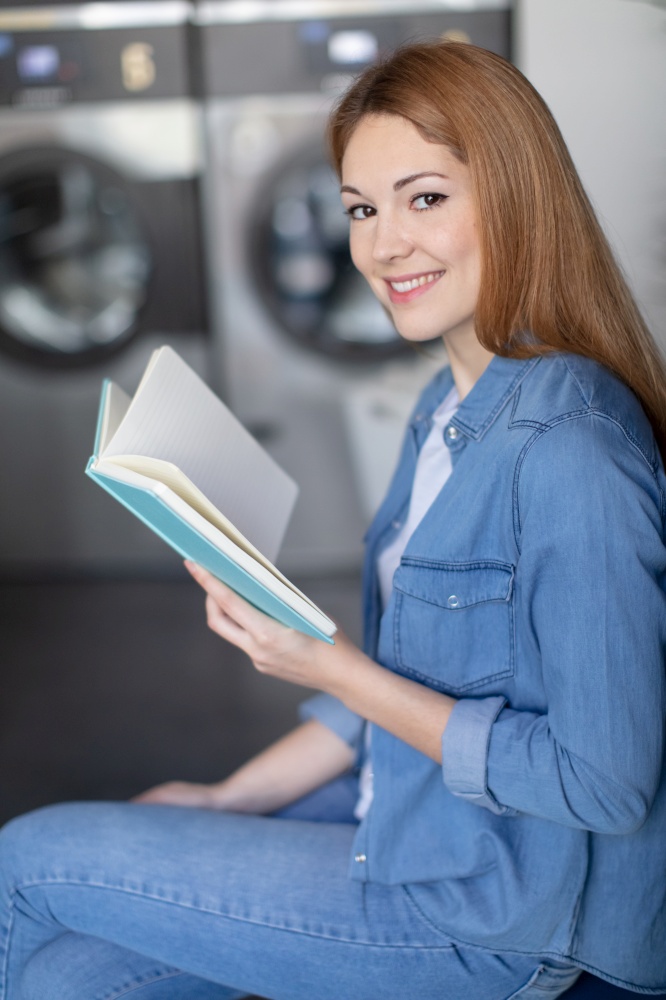 shot of a young woman reading a book in laundromat
