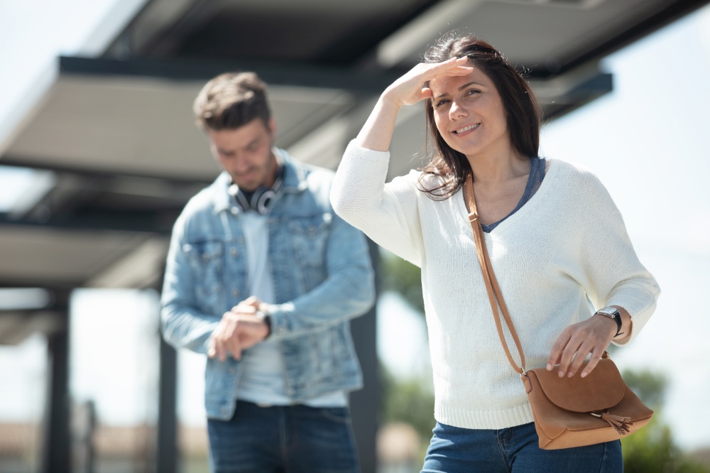 woman waiting for public transport shields eyes from the sun