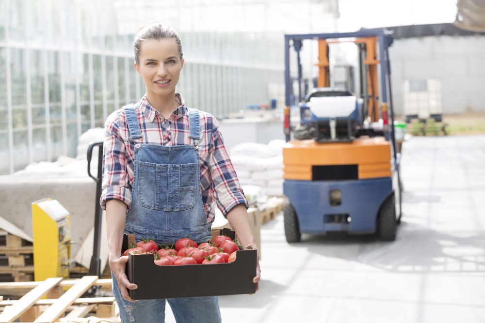 Portrait of smiling farmer with tomatoes in crate against forklift