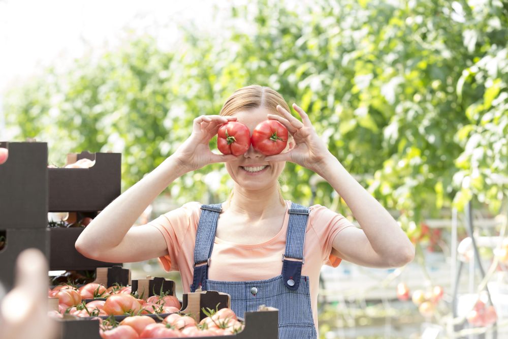 Smiling woman playing with tomatoes while standing in farm