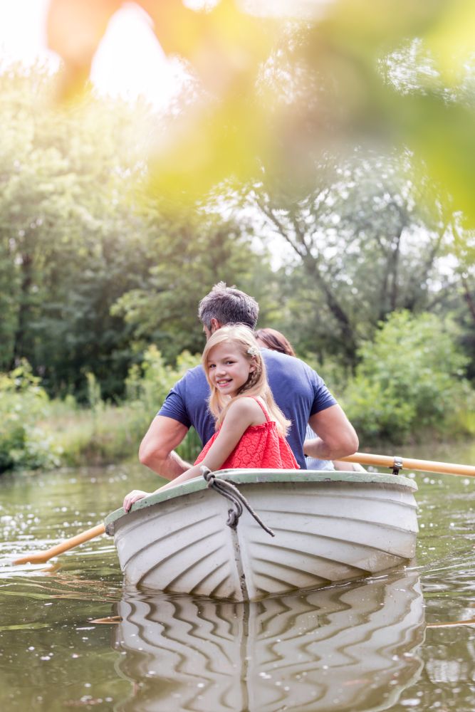 Portrait of cute smiling girl sitting with father on rowboat in lake during summer