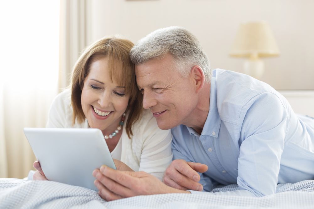 Smiling mature couple sharing digital tablet while lying on bed at home