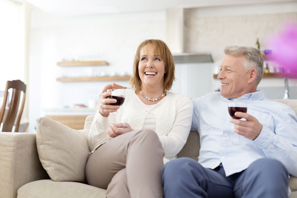 Smiling mature couple sitting on sofa while holding drinks at home