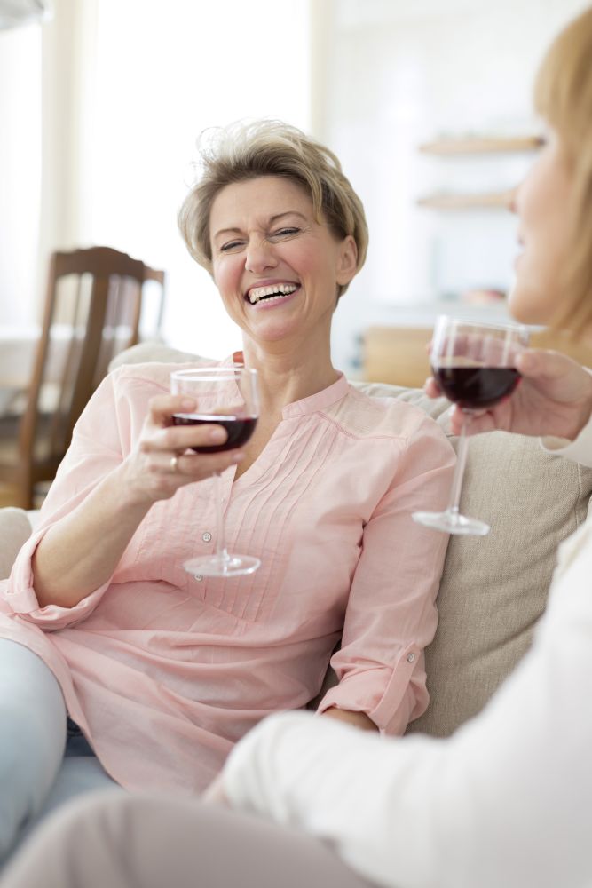 Cheerful mature friends with drinks sitting on sofa at home