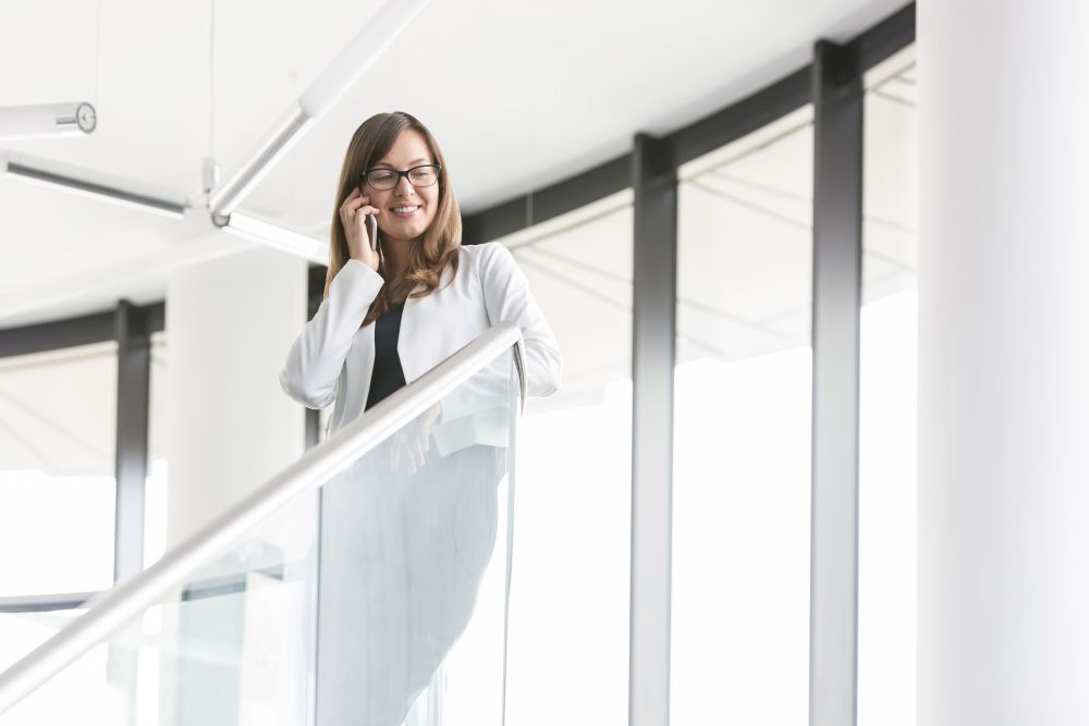 Low angle view of smiling businesswoman talking on smartphone while standing at office