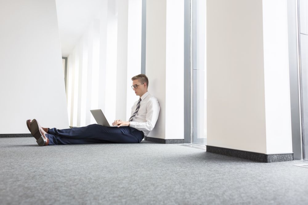 Young businessman using laptop while sitting on floor at office