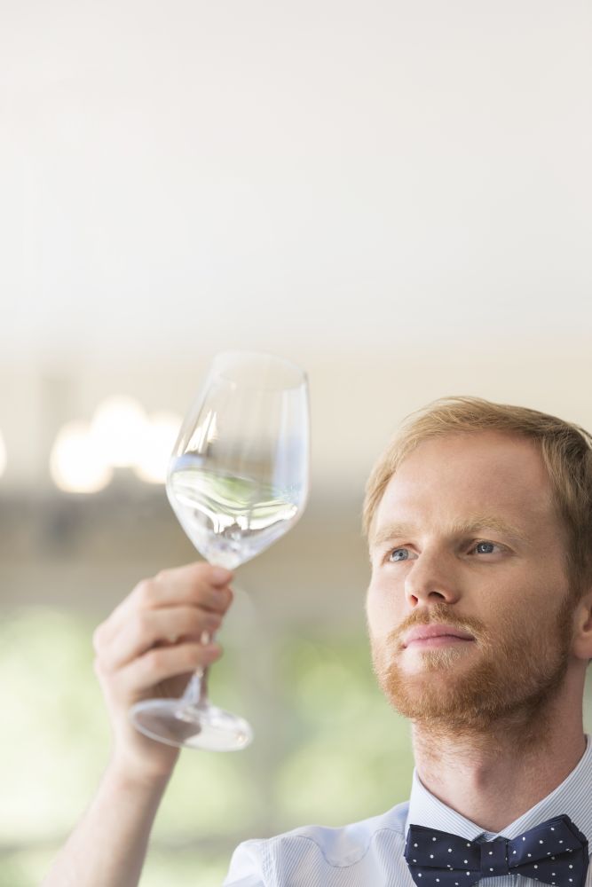 Closeup of young waiter looking at empty wineglass in restaurant