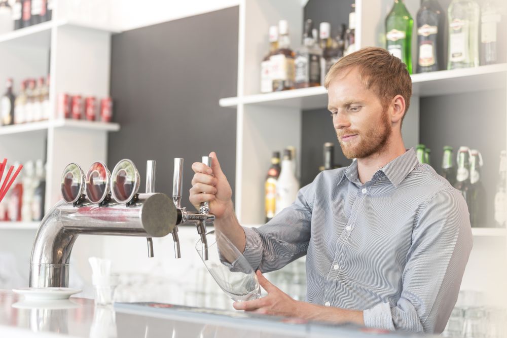 Young waiter filling glass from beer tap at restaurant