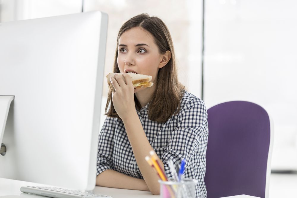 Creative businesswoman eating sandwich while sitting at computer desk