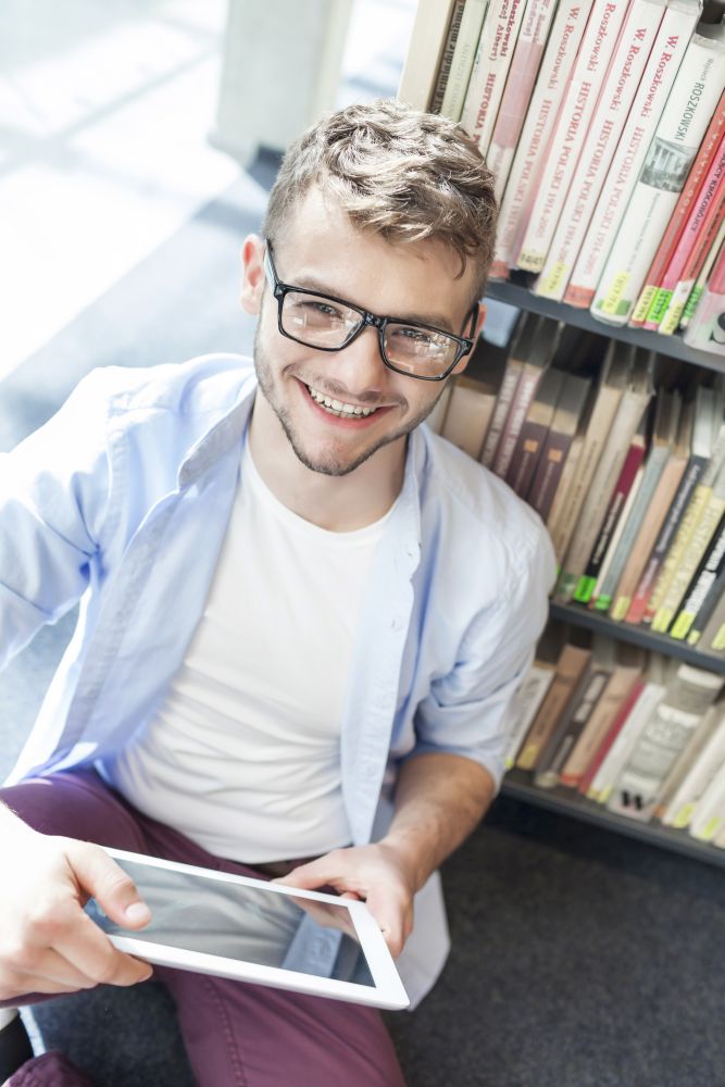 High angle portrait of smiling young man using digital tablet at library