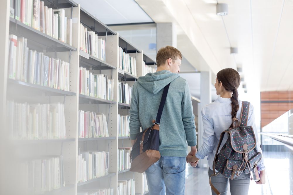 Rear view of couple walking while holding hands in library