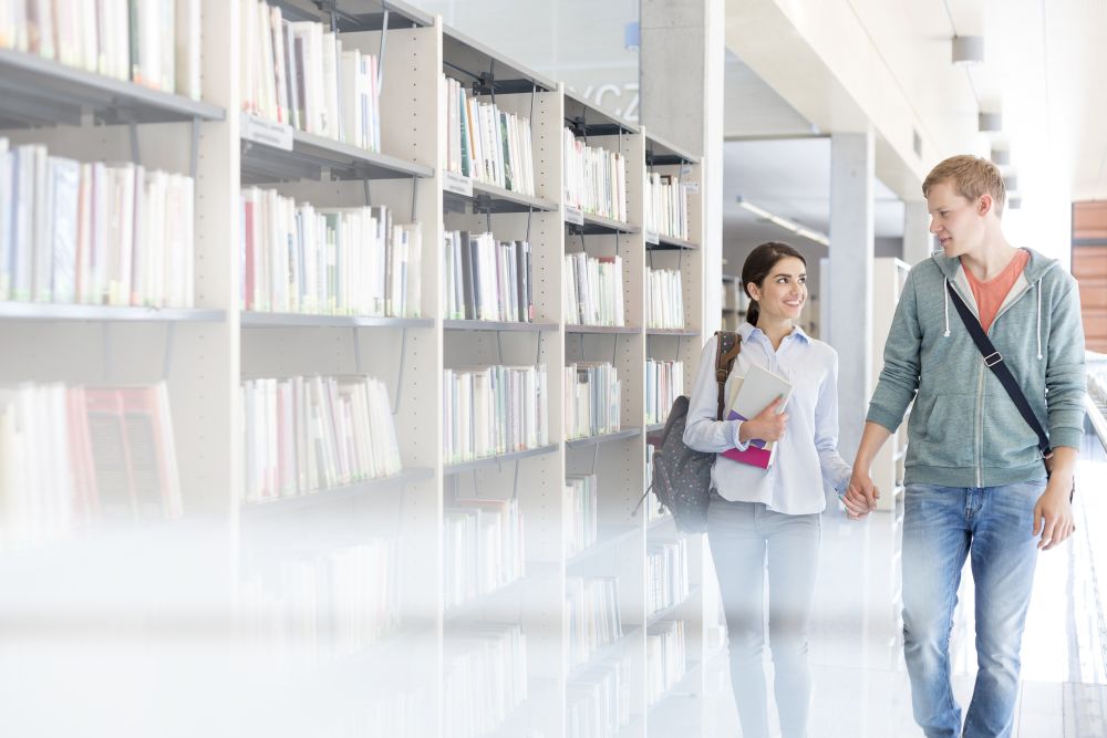 Couple holding hands while walking by bookshelf in library