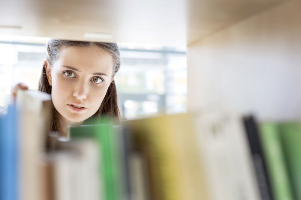 Closeup of young student searching book on shelf at library