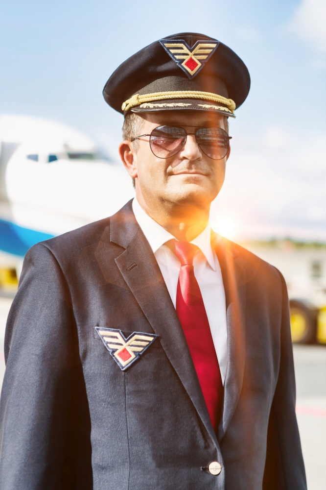 Portrait of mature pilot standing against airplane in airport