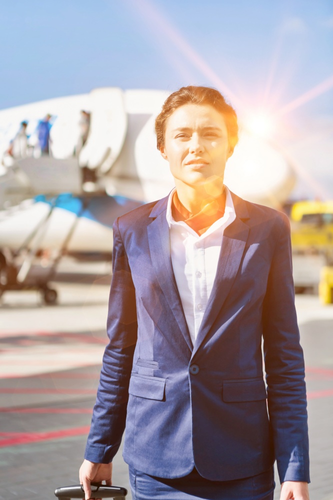 Portrait of young attractive flight attendant standing against airplane in airport