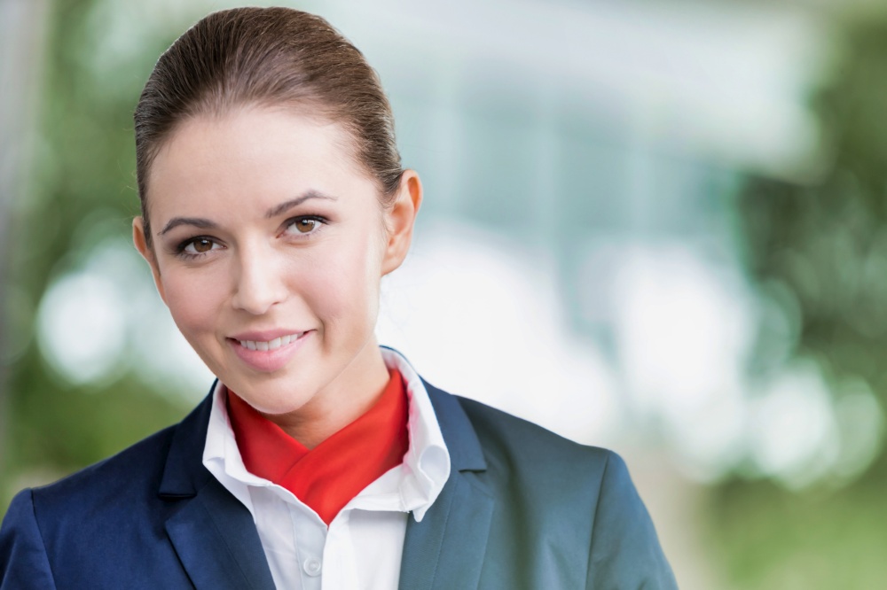 Portrait of young attractive flight attendant standing against flight display monitor in airport