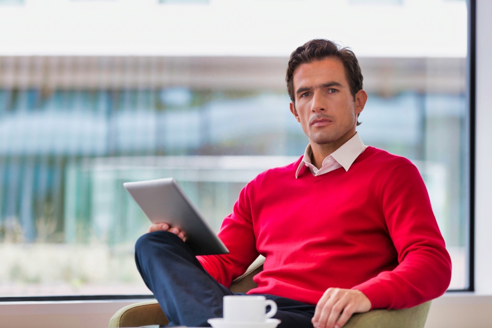 Portrait of attractive businessman using digital tablet while sitting and drinking coffee in lobby