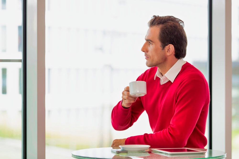 Portrait of thougtful businessman sitting while drinking coffee in lobby