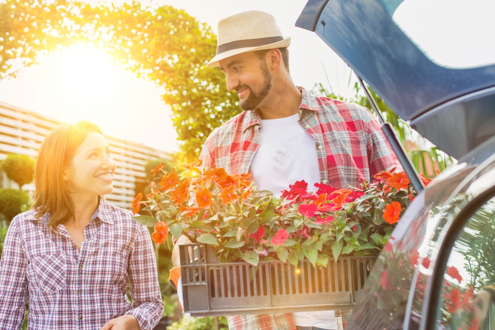 Portrait of mature gardener putting flowers on car trunk while talking to woman in garden shop