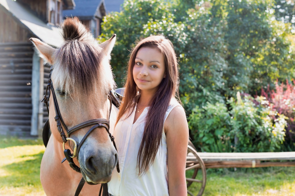 Portrait of young beautiful woman standing with horse in ranch