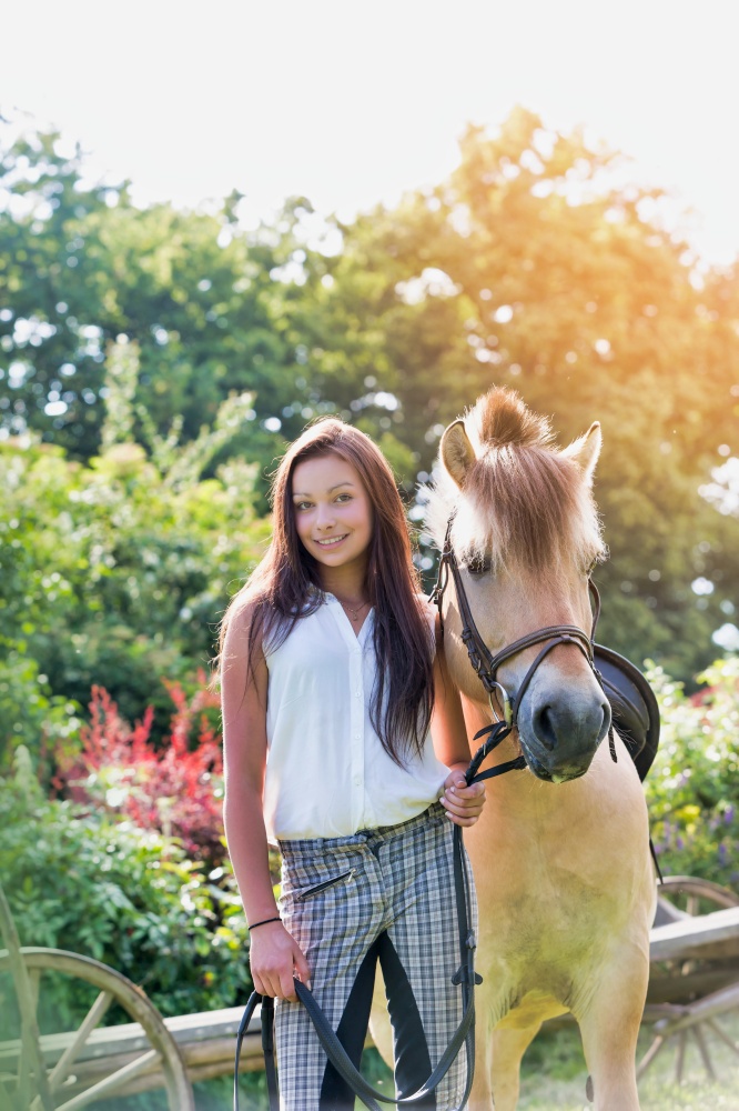 Portrait of young beautiful woman standing with horse in ranch