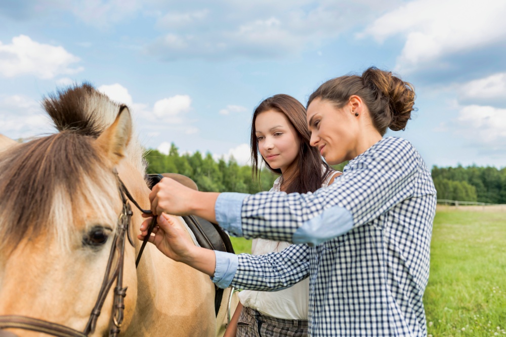 Portrait of mature woman teaching young woman on how to pull horse bit
