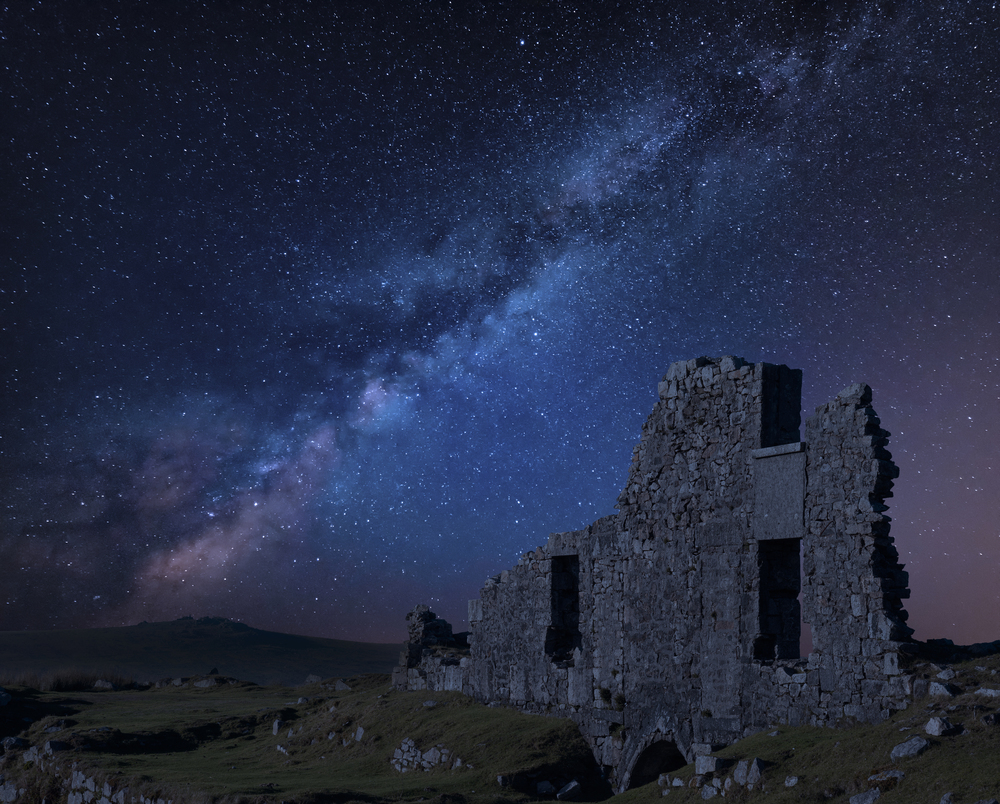 Stunning vibrant Milky Way composite image over abandoned Foggintor Quarry in Dartmoor with raking soft sunlight over ruins and derelict buildings