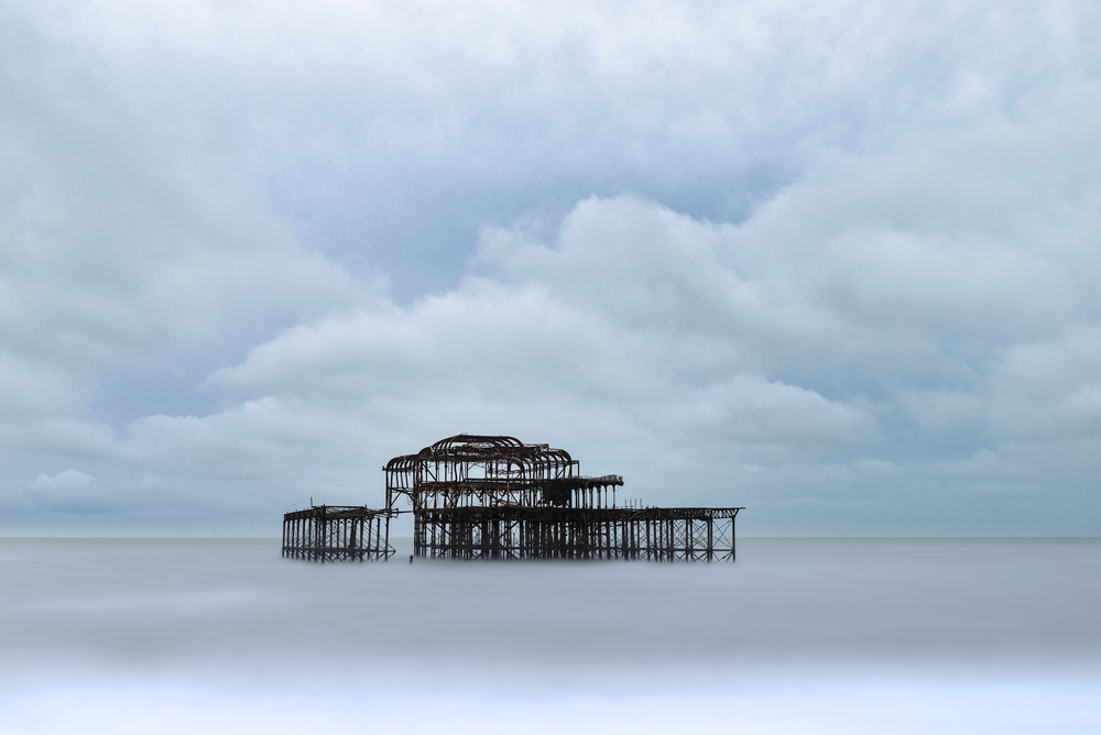 Landscape image of derelict Victorian West Pier at Brighton in West Sussex with moody evening sky
