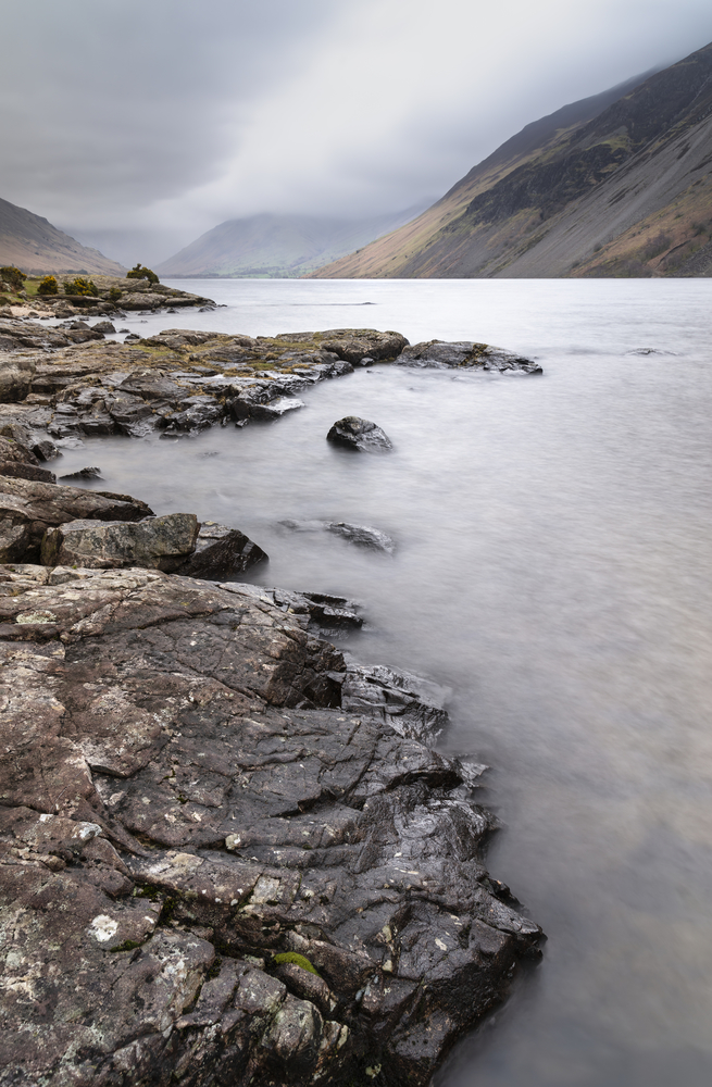 Beautiful long exposure landscape image of Wast Water in UK Lake District during moody Spring evening