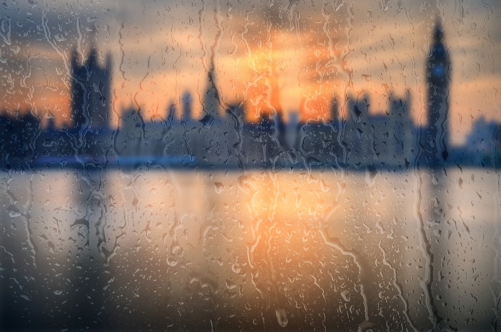 Beautiful landscape conceptual view of London City through glass window with raindrops running down the glass. Big Ben and Houses of Parliament London during Winter sunset.