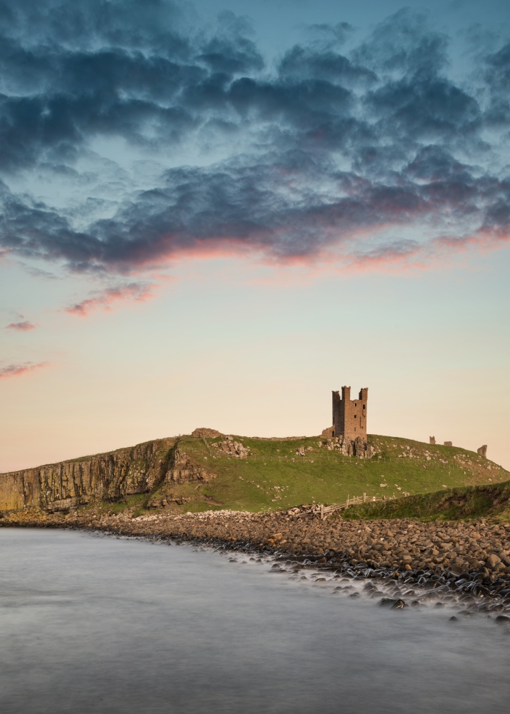 Beautiful landscape image of Dunstanburgh Castle on Northumberland coastline in England during late Spring evening