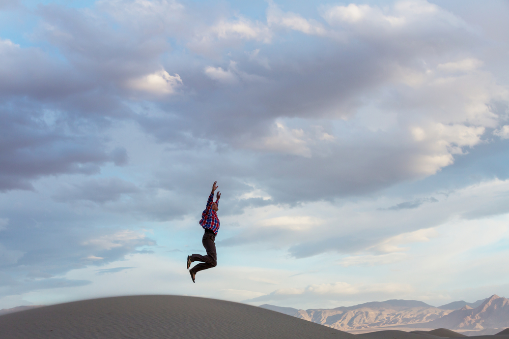 Jumping man in sand dunes at sunset