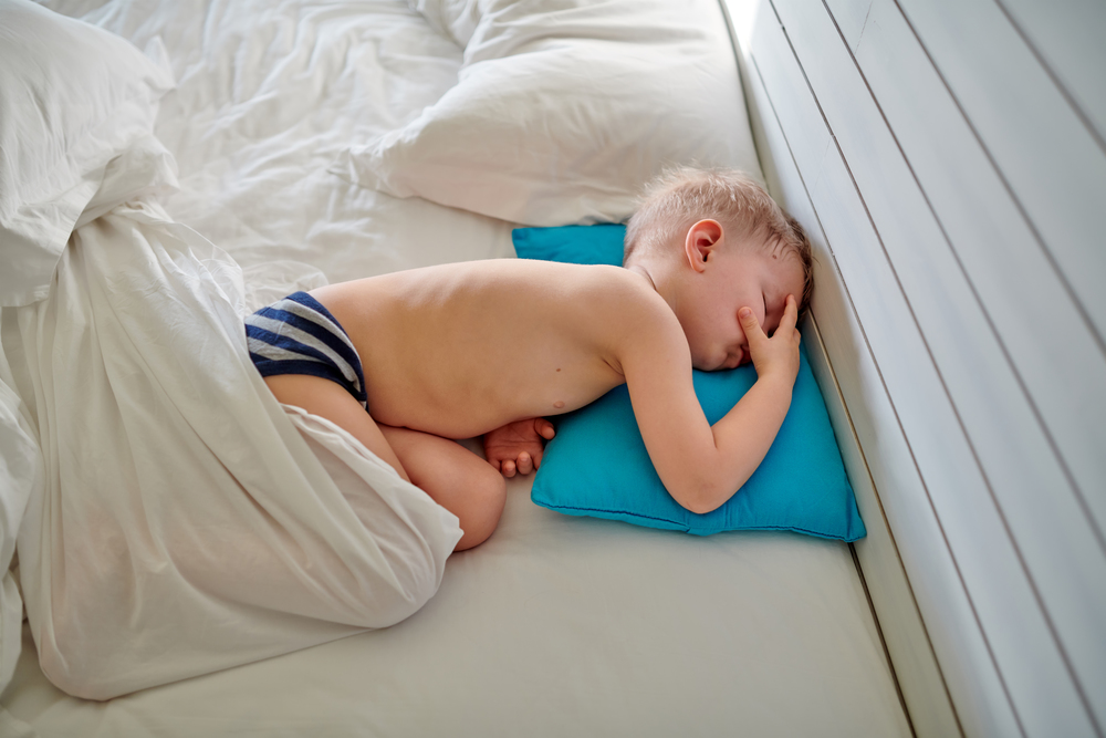 Three year old toddler boy sleeping on blue pillow under blanket