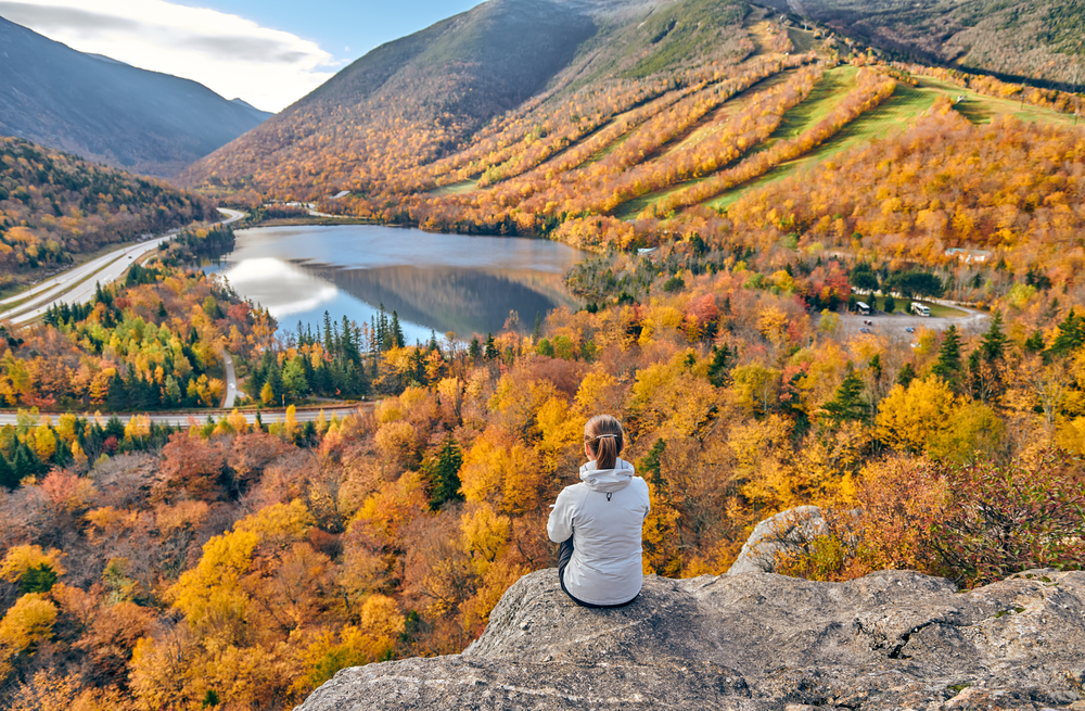 Woman hiking at Artist&rsquo;s Bluff in autumn. View of Echo Lake. Fall colours in Franconia Notch State Park. White Mountain National Forest, New Hampshire, USA