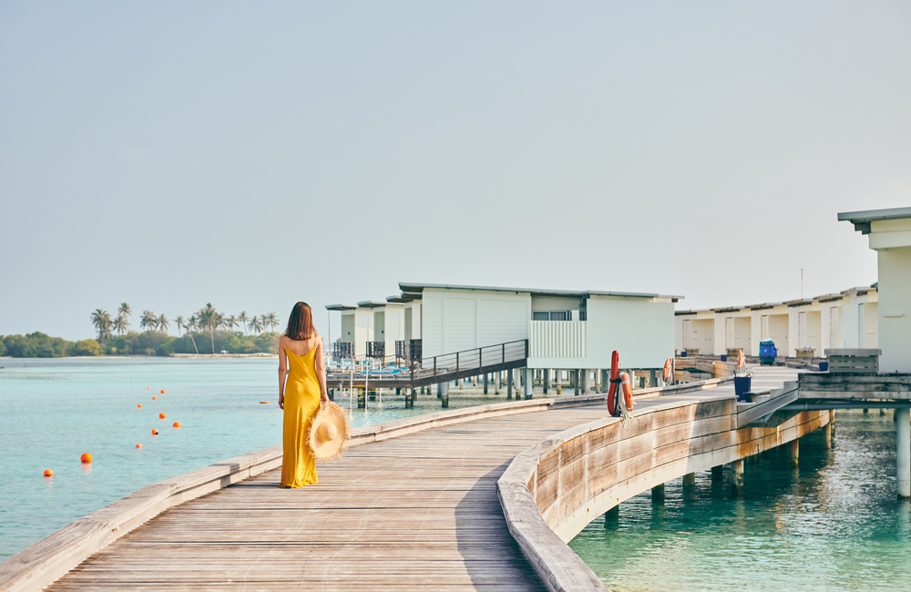 Woman in dress walking on tropical beach boardwalk. Summer vacation at Maldives.