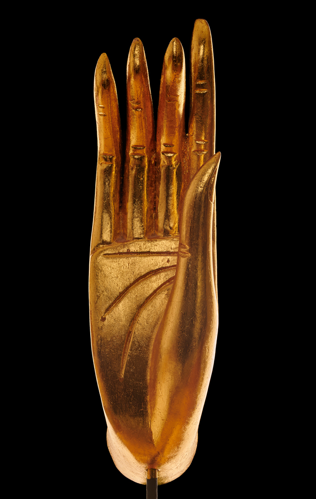 Close up of golden hand of Buddha statue over black background