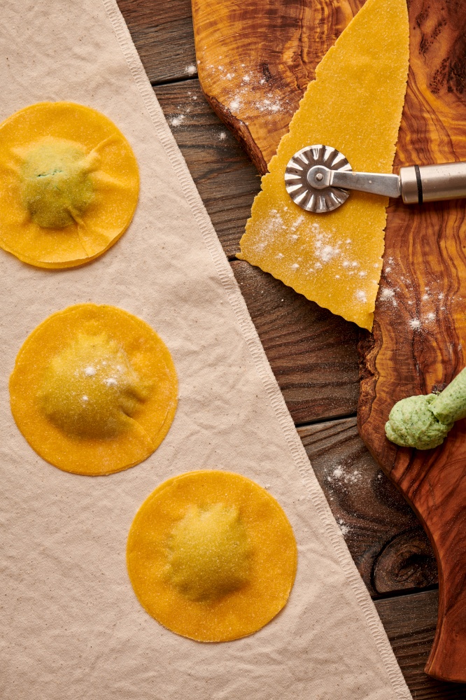 Tasty raw homemade ravioli pasta with spinach and ricotta on wooden rustic background. Process of making Italian ravioli.