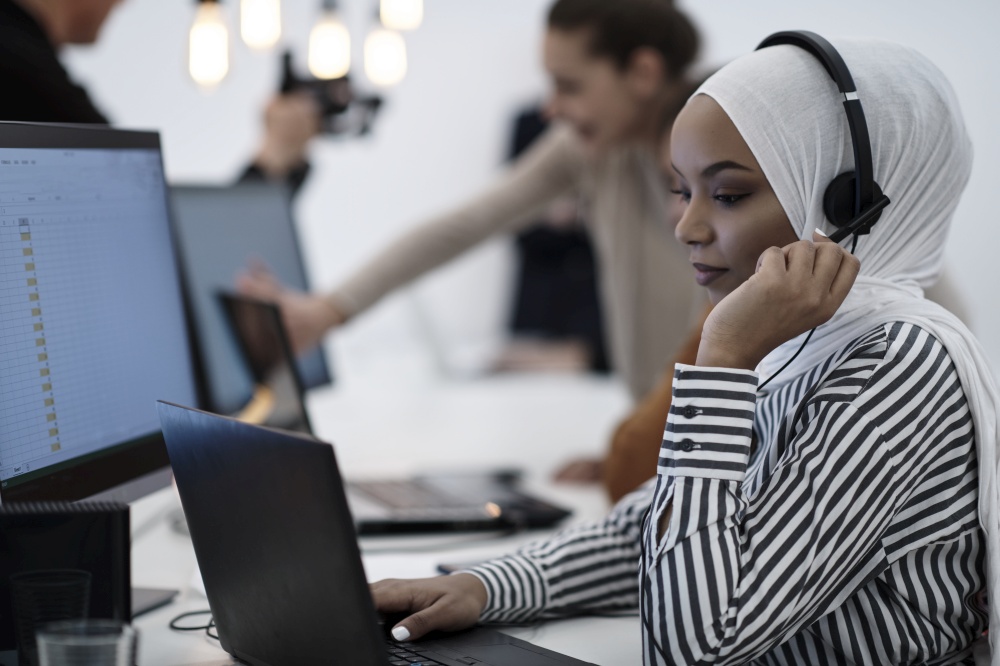 beautiful modern african Muslim businesswoman in office, wearing hijab speaking on headset at modern startup coworking space