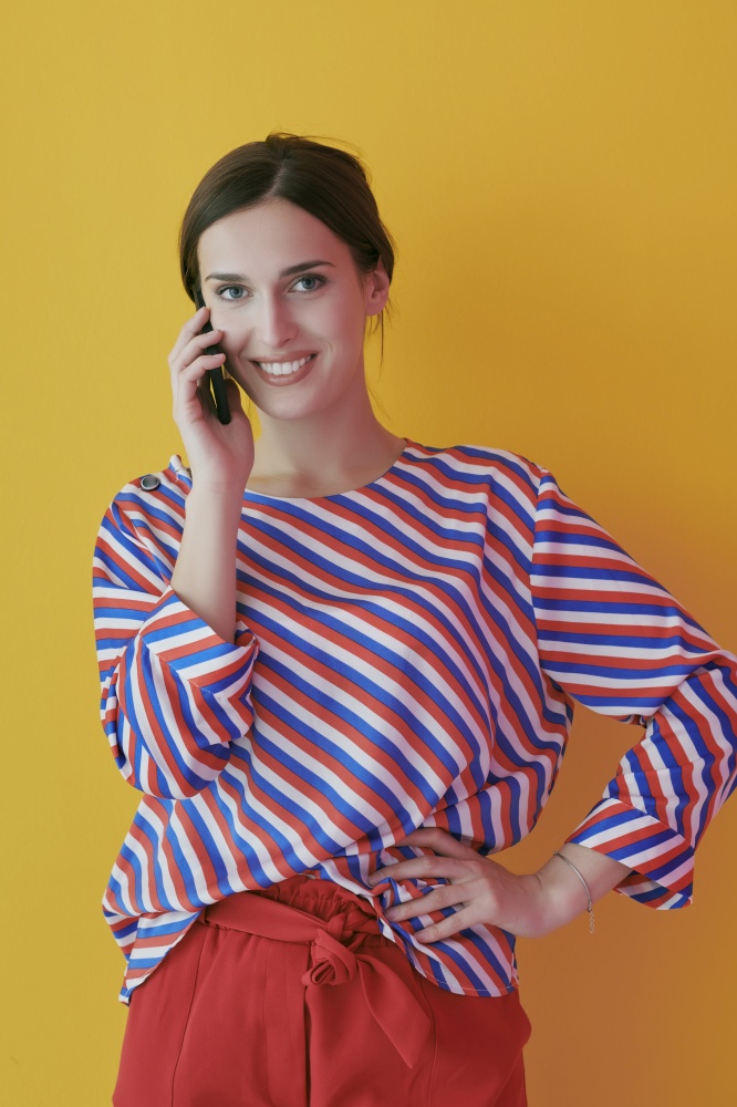 Portrait of young girl talking on the phone while standing in front of yellow background. Female model representing modern fashion and technology concept
