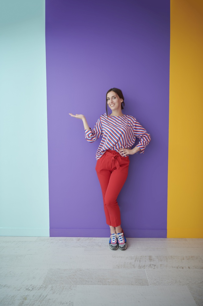 Portrait of happy smiling young beautiful woman in a presenting gesture with open palm isolated on colorful background. Female model in modern fashionable clothes posing in the studio