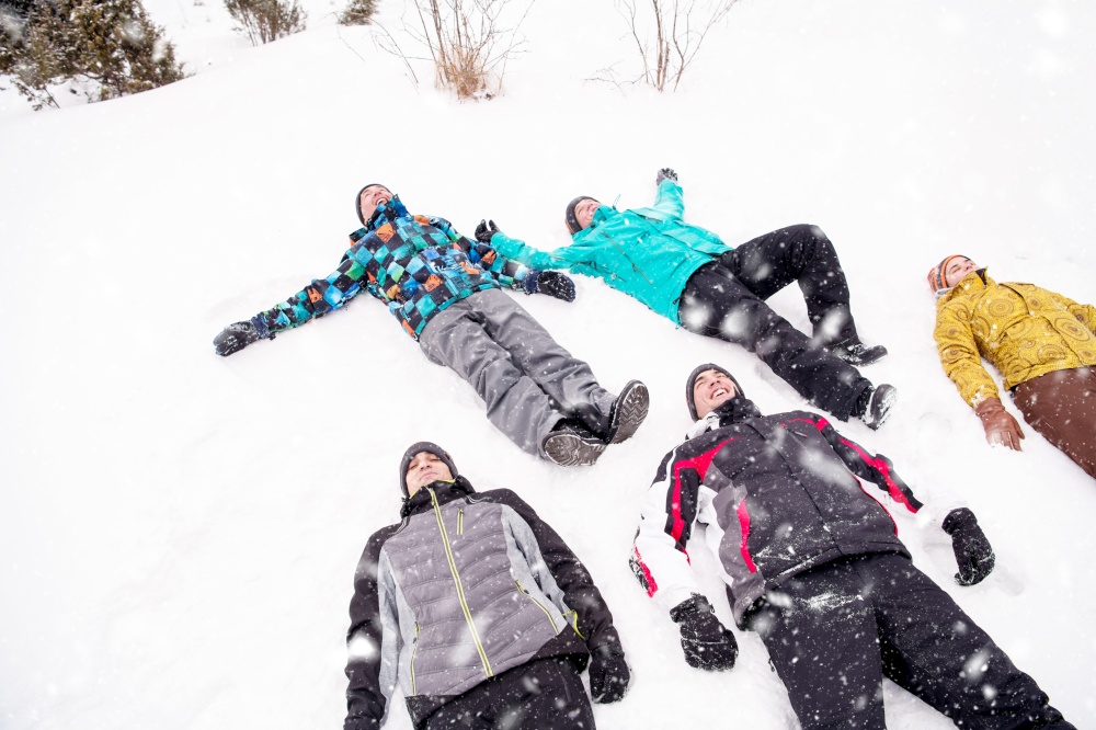 group of young happy business people laying on snow and making snow angel while enjoying snowy winter day with snowflakes around them during a team building in the mountain forest