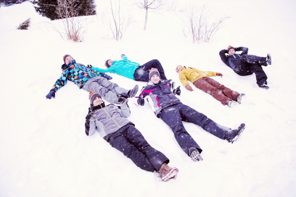 group of young happy business people laying on snow and making snow angel while enjoying snowy winter day with snowflakes around them during a team building in the mountain forest