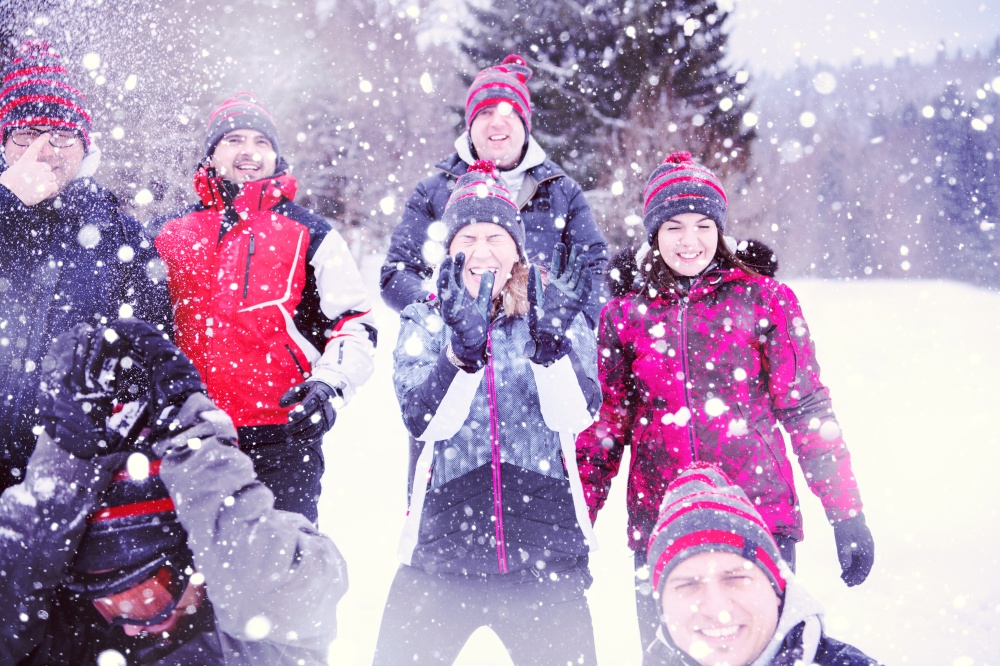group of young happy business people having fun throwing snow in the air while enjoying snowy winter day with snowflakes around them during a team building in the mountain forest