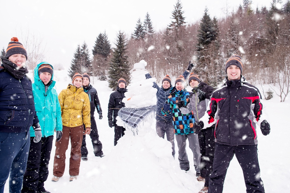 group portrait of young happy business people after a competition posing with finished snowman while enjoying snowy winter day with snowflakes around them during a team building in the mountain forest