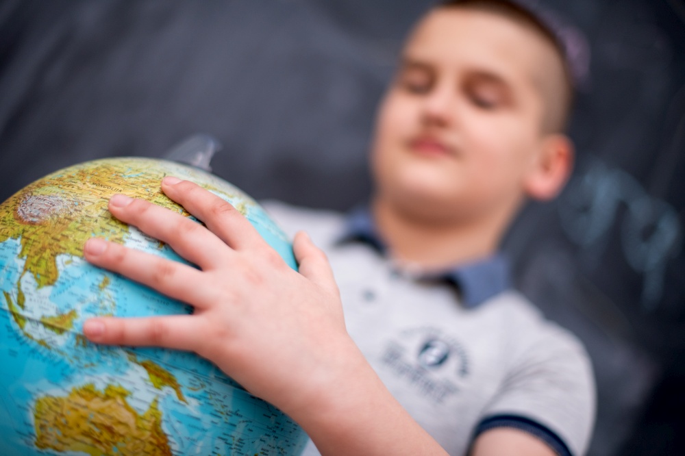 happy cute boy learning about the world using globe of earth while standing in front of black chalkboard