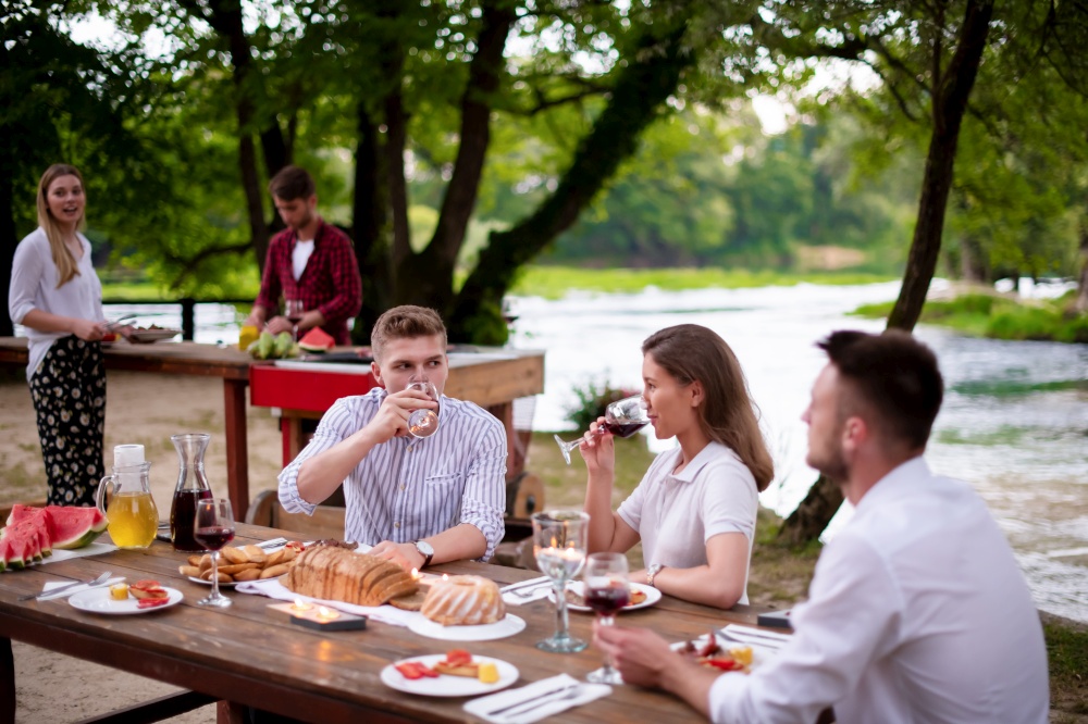 group of happy friends having picnic french dinner party outdoor during summer holiday vacation  near the river at beautiful nature